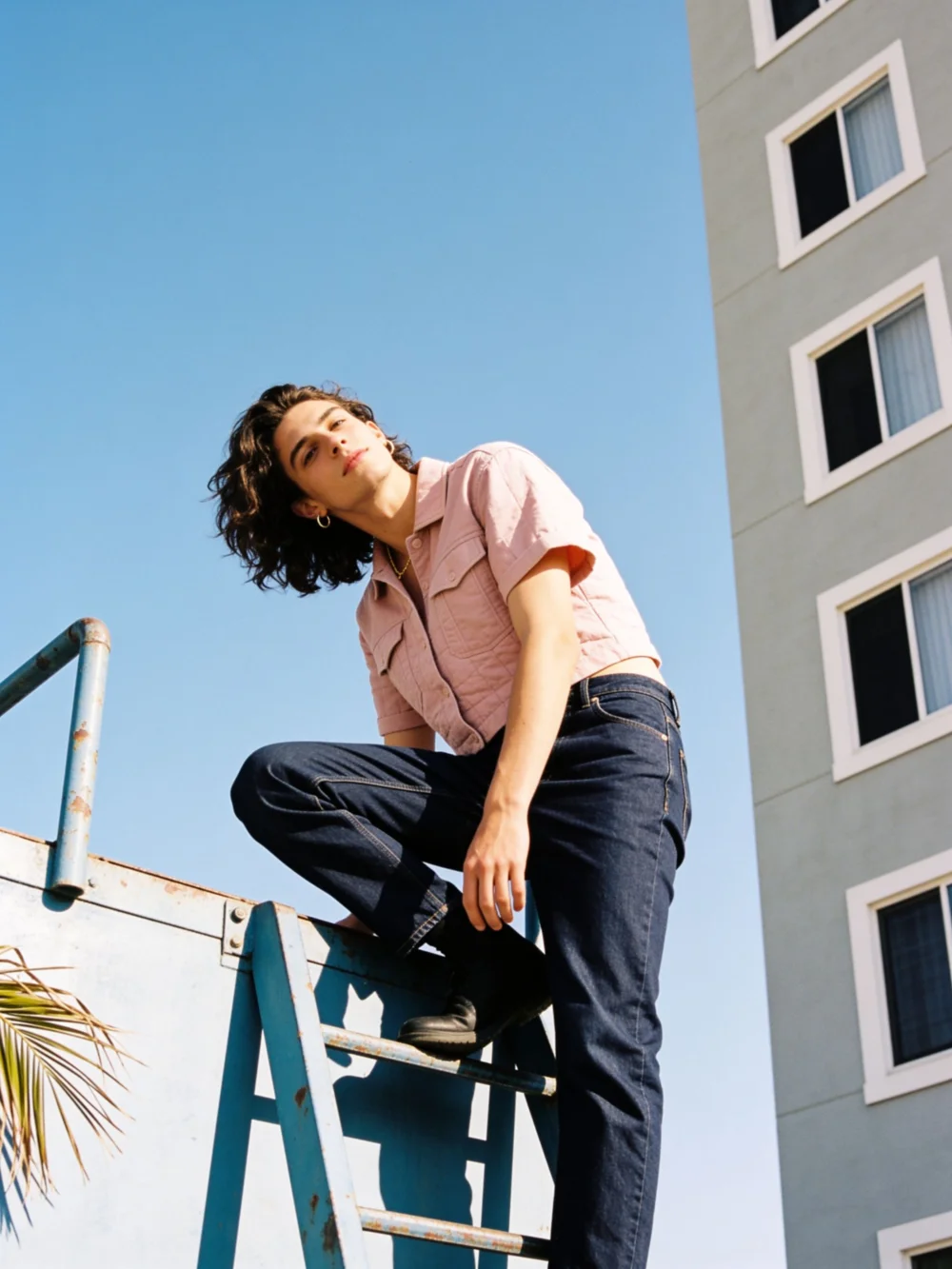 AI fashion model photo example: man in a pink boxy shirt and navy jeans, teal ladder city scene